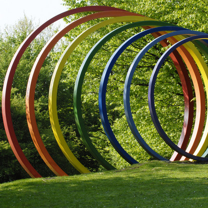 Large colorful steel spectral rings stand on green lawn.